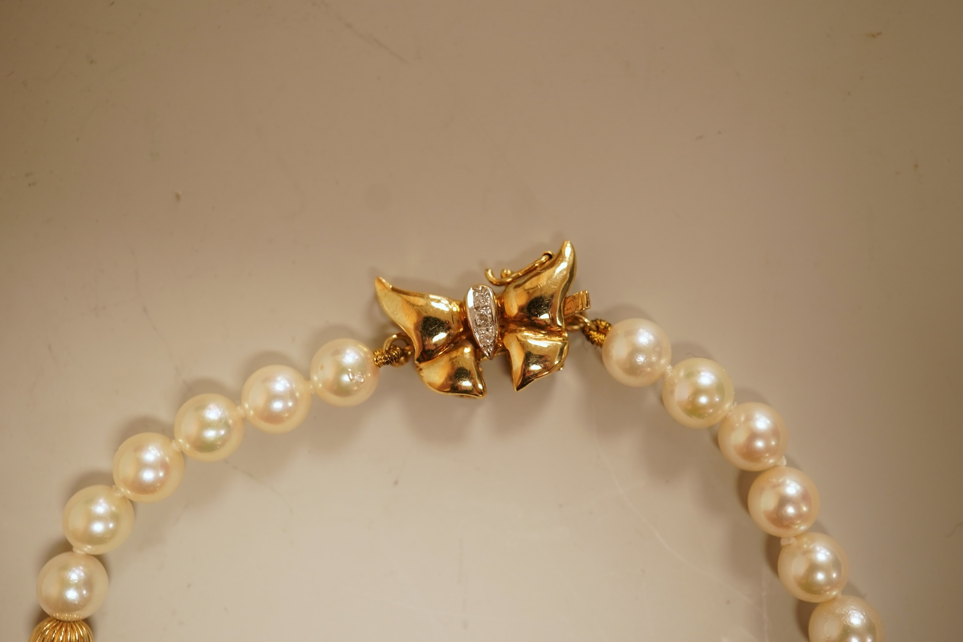 A modern twin strand cultured pearl choker necklace, with an engraved 9ct clasp, approx. 40cm, together with a cultured pearl bracelet, with diamond chip set butterfly shaped 14k clasp, 18cm, with four fluted yellow meta